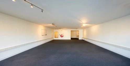 Lege, langwerpige kantoorruimte aan de Hoogte Kadijk met witte muren en donker tapijt.